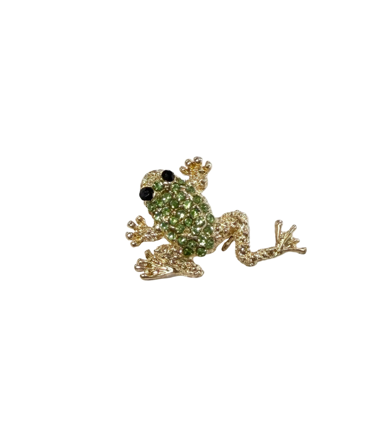 A small frog-shaped brooch with a green rhinestone-covered body and gold-toned limbs and feet, placed on a white surface with handwritten notes in the background.